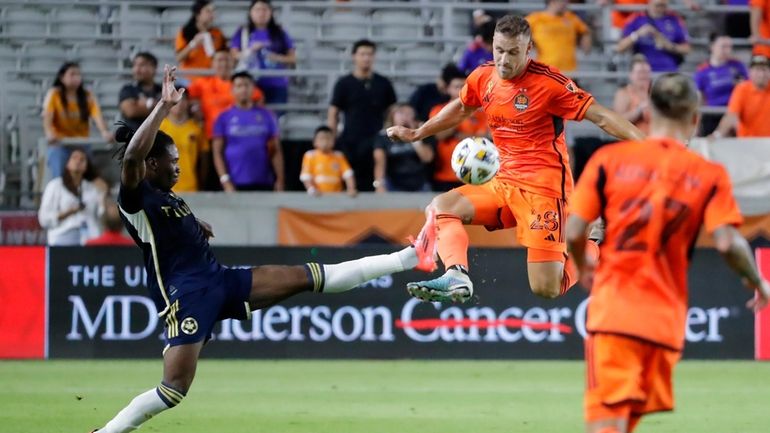 Vancouver Whitecaps defender Sam Adekugbe, left, kicks away as Houston...