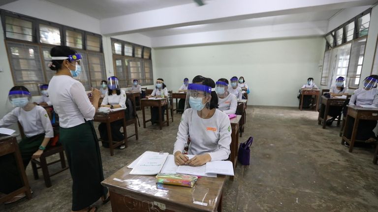 A teacher and students wearing face shields and masks attend...