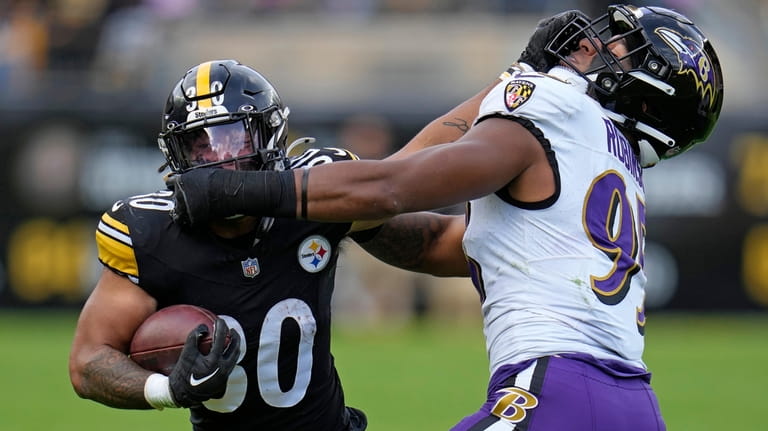 Pittsburgh Steelers running back Jaylen Warren (30) stiff-arms Baltimore Ravens...