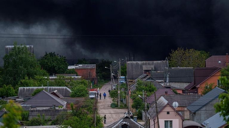 People walk on a street while smoke rises after a...