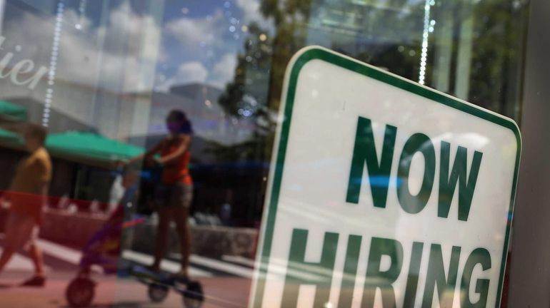 A ''Now Hiring'' sign is seen in a store front...