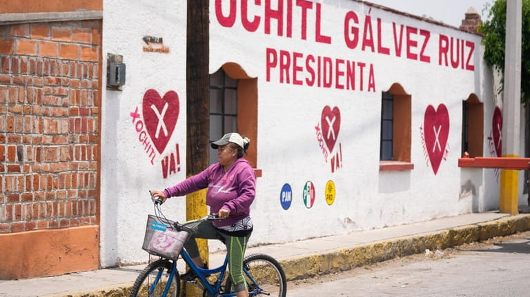 A woman rides her past a political mural promoting presidential...