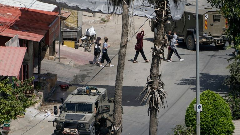 Israeli soldiers arrest a Palestinian man as others walk by...