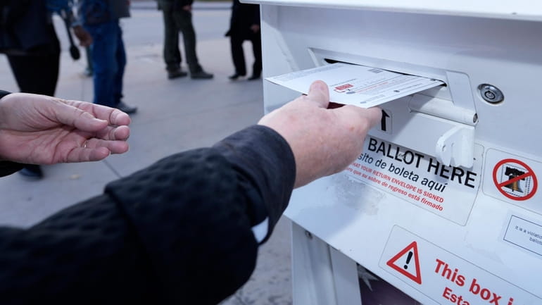 A voter places a ballot in a drop box outside...