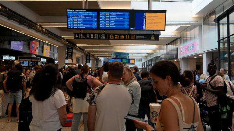 Travelers check trains on an electronic board at the Gare...