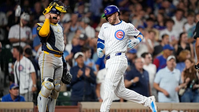 Chicago Cubs' Ian Happ, right, scores in front of Milwaukee...