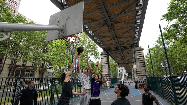 Youths play basketball on a court under an aerial metro...