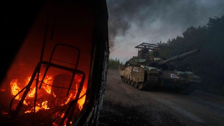 A Ukrainian tank passes by a burning car near the...