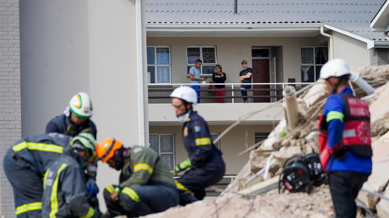Residents watch rescue workers search the site of a building...
