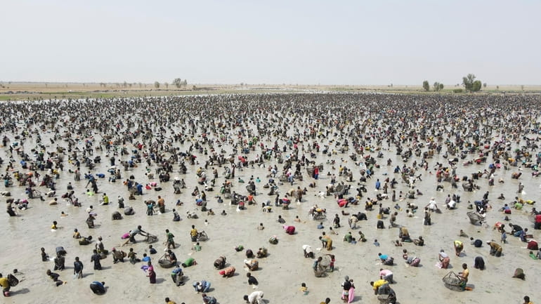 Thousands of fishermen fill a large muddy pond and cast...