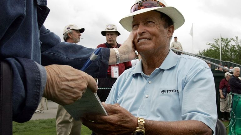 Chi Chi Rodriguez, of Puerto Rico, smiles while signing an...