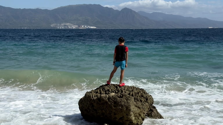 A boy stands on a rock on Verde Island opposite...