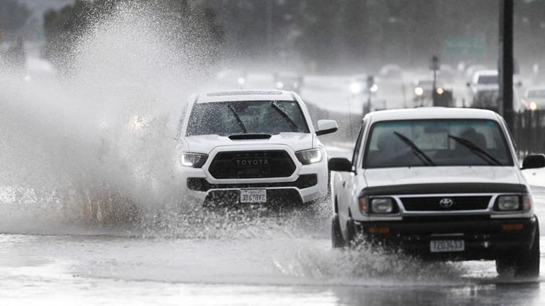 Trucks drive down a flooded street, Tuesday, Feb. 6, 2024,...