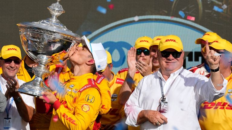 Alex Palou, front left, kisses his trophy as he celebrates...