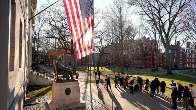 People take photos near a John Harvard statue, left, on...