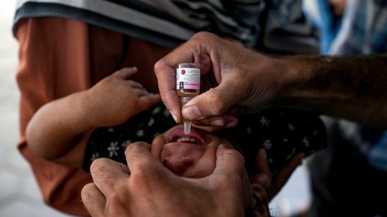 A health worker administers a polio vaccine to a child...