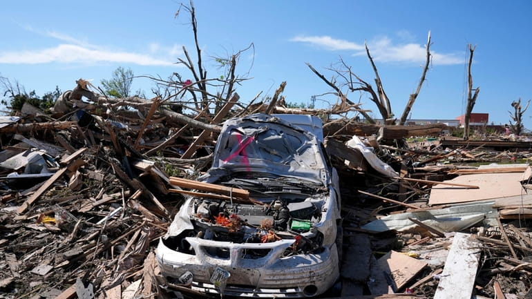 A tornado damaged car sits in a pile of debris,...