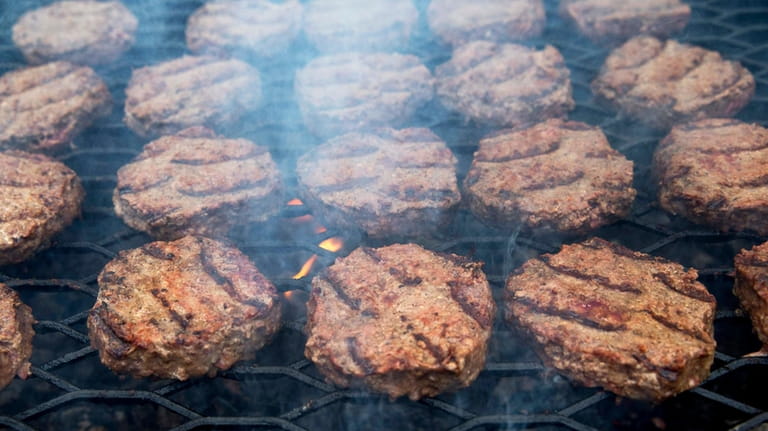 Smoke wafts up as hamburgers are cooked on a grill...