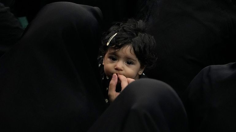 An Iranian Shiite Muslim woman feeds her child as they...