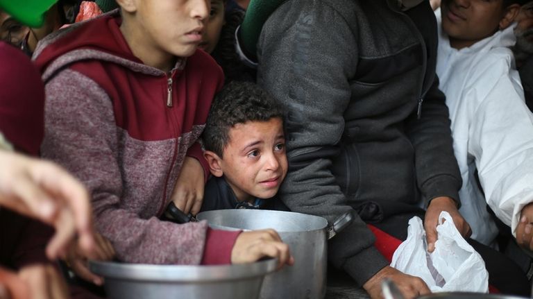 Palestinians line up for free food distribution during the ongoing...