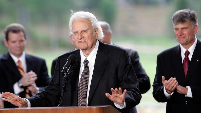 Billy Graham speaks as his son Franklin Graham, right, listens...