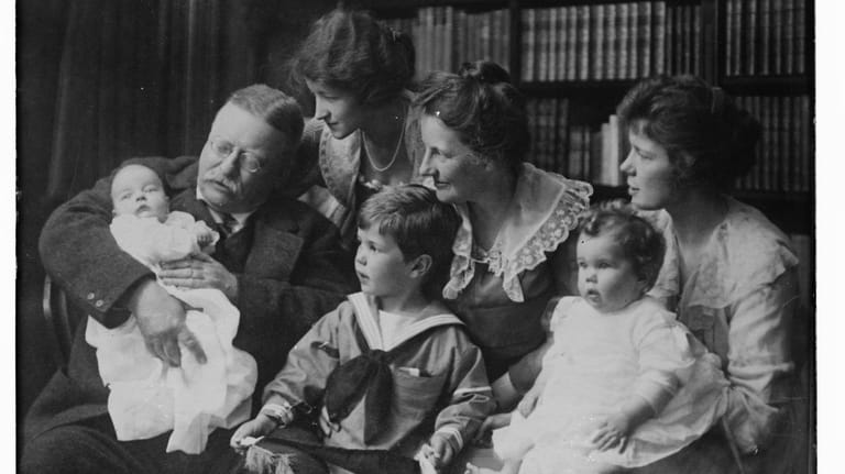 Theodore Roosevelt holds a baby as wife, Edith, Mrs. Archie Roosevelt,...