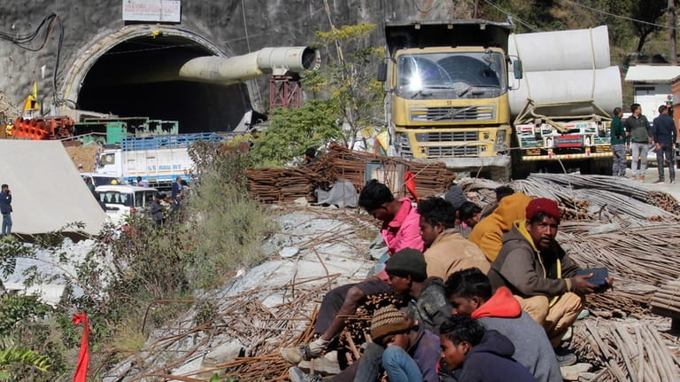 People sit near the site of an under-construction road tunnel...