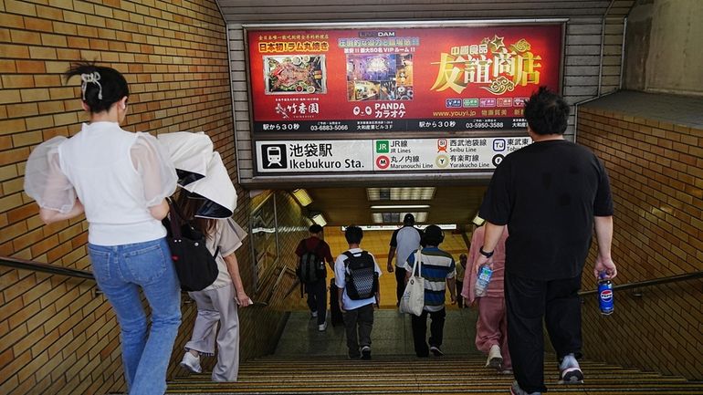 Commuters walks past advertisements of Chinese restaurant and karaoke which...