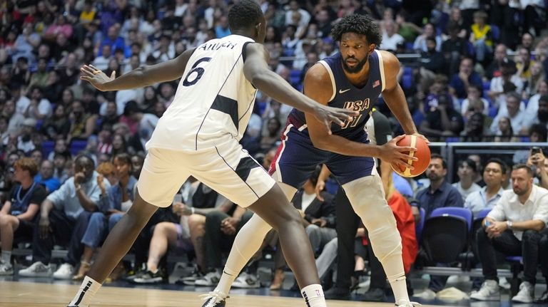 United States' center Joel Embiid, right, looks to pass as...