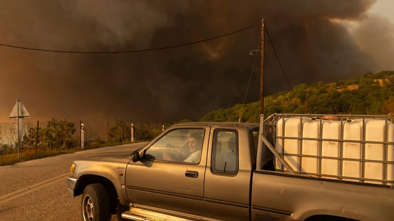 A man drives away as flames burn a forest during...