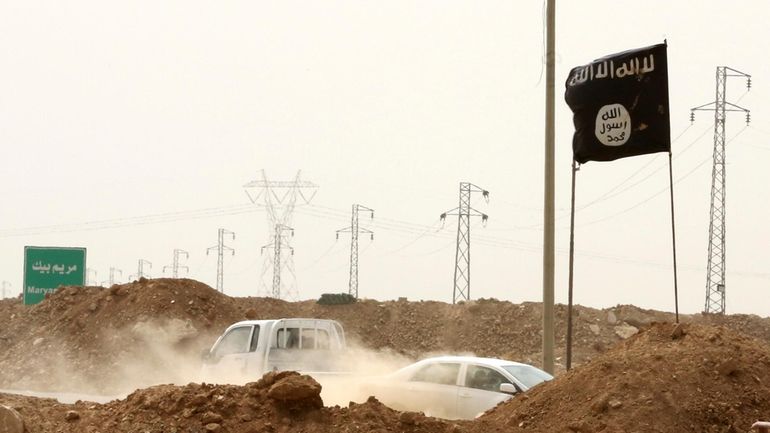 Islamic State militants pass a checkpoint bearing the group's trademark...