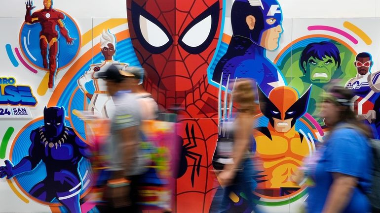 Convention attendees blur past a wall of illustrated Marvel superhero...