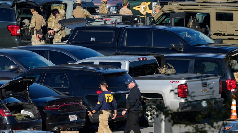 Law enforcement personnel are staged in a school parking lot...