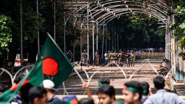 Military and paramilitary personnel stand guard as protesters block the...