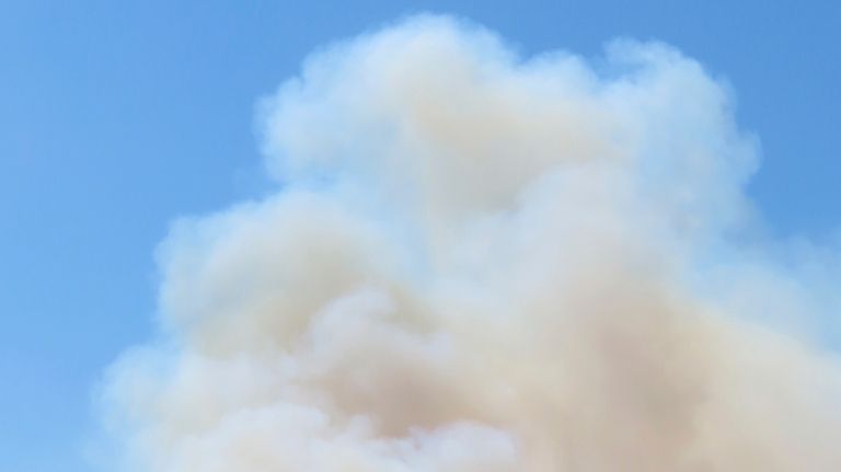 Large plumes of smoke rise from a forest fire in...