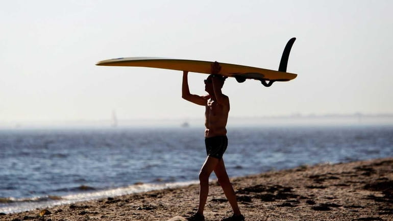 A windsurfer carries his board to the water to get...
