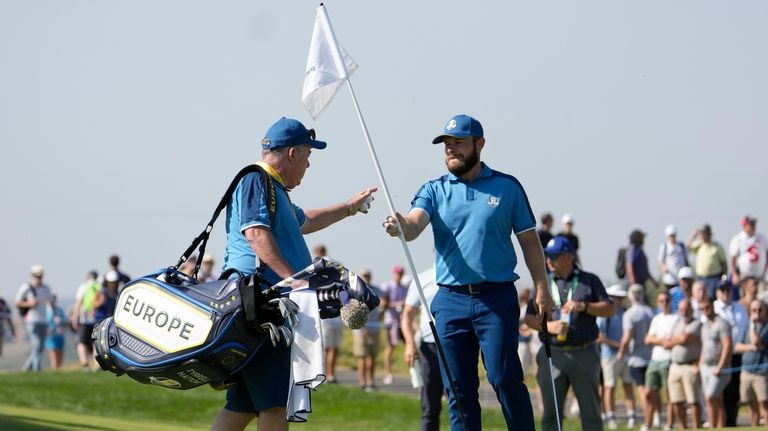 Europe's Tyrrell Hatton, right hand the pin flag to his...