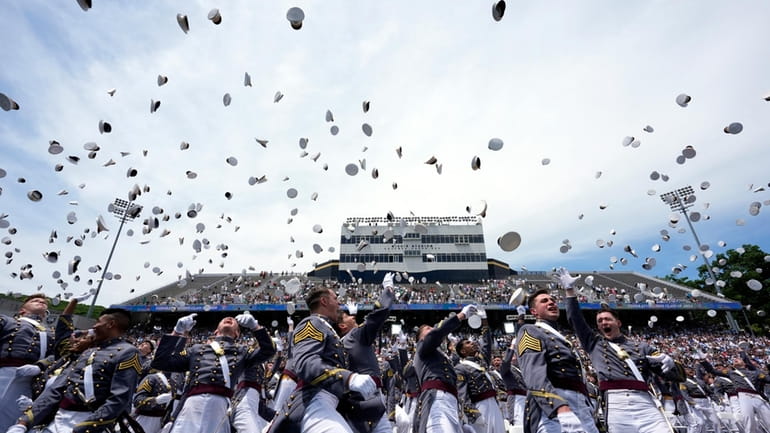 West Point graduates toss their caps into the air at...