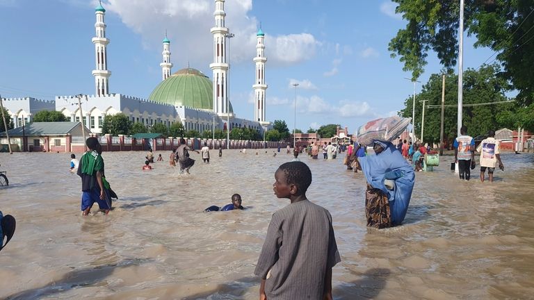 People walk through floodwaters following a dam collapse in Maiduguri,...