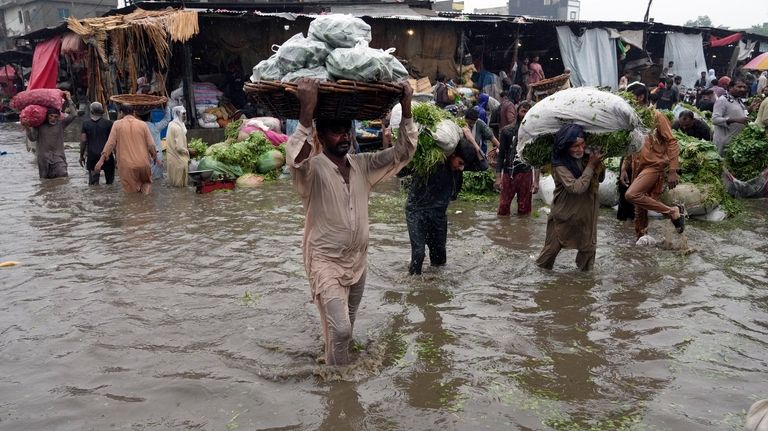 People carry vegetables through a flooded road caused by heavy...