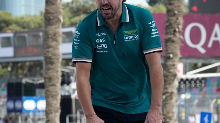 Aston Martin driver Fernando Alonso of Spain rides a scooter...