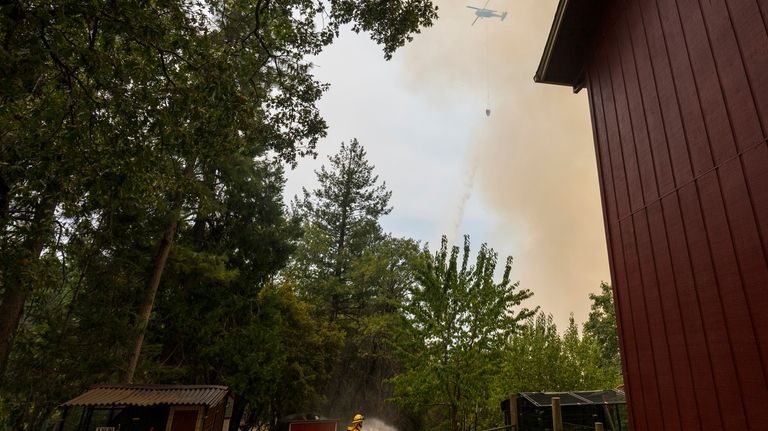 Volunteer firefighter Craig Klieb sprays water around his house as...