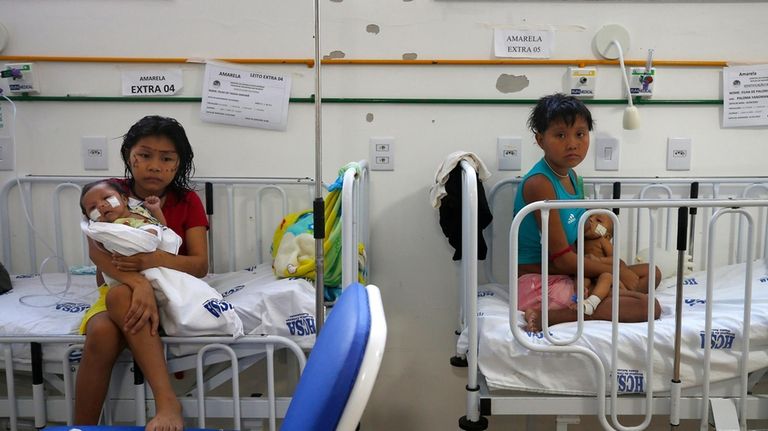 Yanomami women hold their babies receiving medical treatment at the...