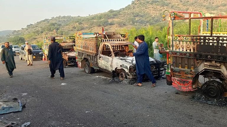 People look burnt vehicles, torched by gunmen after killing passengers,...