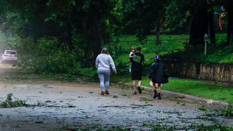 A family walks along a street littered with downed tree...