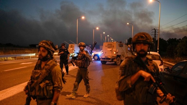 Israeli soldiers block a road backdropped by smoke from a...