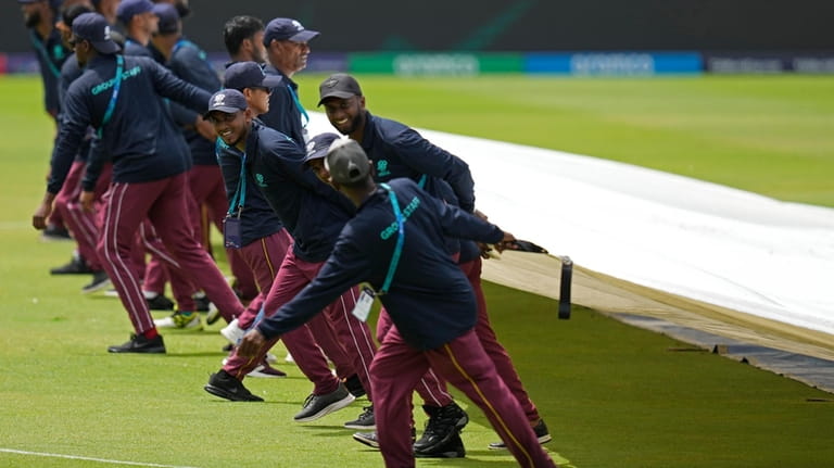 Groundsmen pull the covers as umpires inspect the field after...