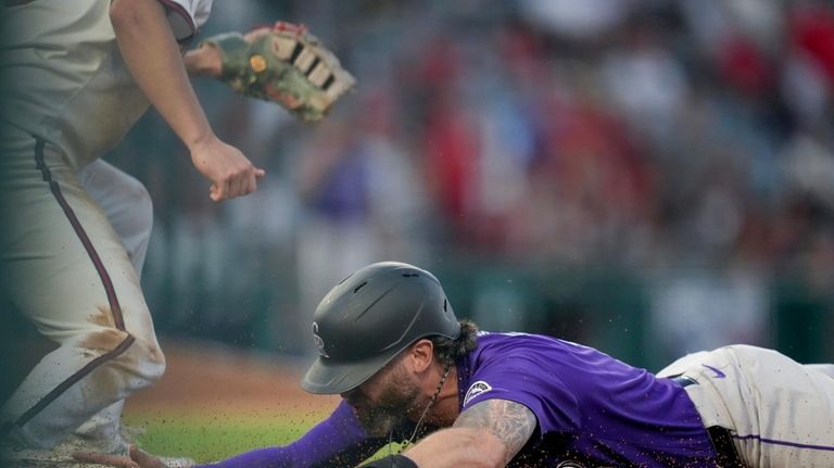 Colorado Rockies' Jake Cave slides into first base during the...