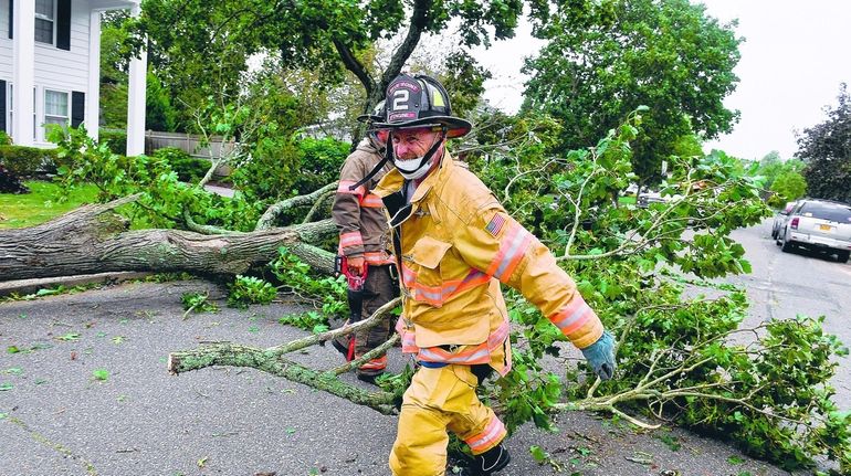 Firefighters from the Blue Point Fire Department remove branches from...