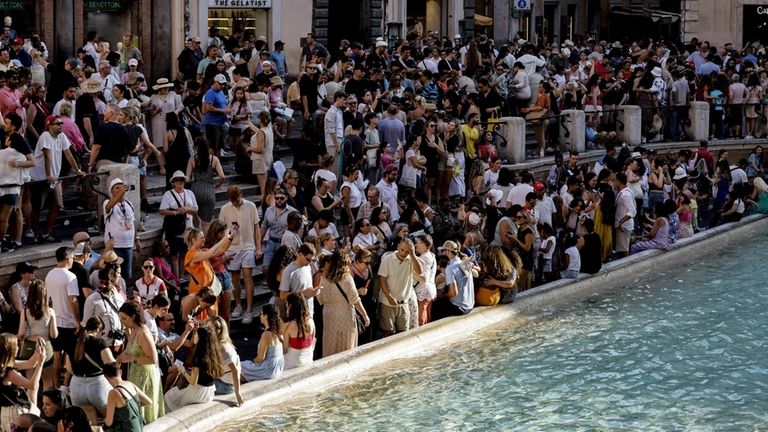 Tourists gather in front of Trevi Fountain during a hot...